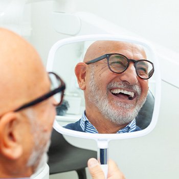 Man with glasses smiling at reflection in handheld mirror