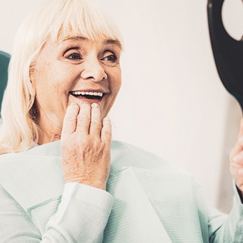 A senior woman admiring her dentures in a hand mirror
