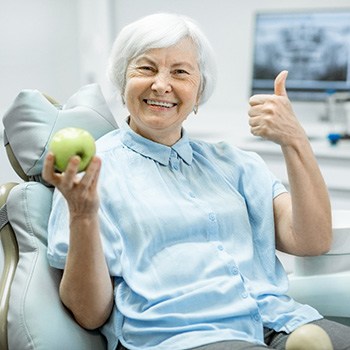 An older woman holding a green apple in a dentist’s office