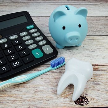 A toothbrush, a calculator, a piggy bank, and a model tooth sitting on a wooden table