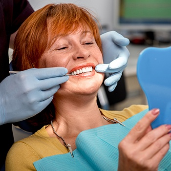 Senior woman in dental chair looking at smile in mirror