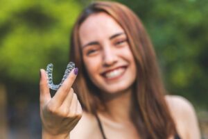 Woman smiling while holding up her Invisalign tray