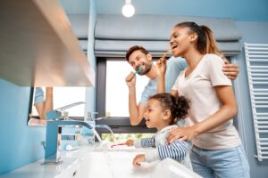 Man, woman, and girl brushing teeth at bathroom sinks